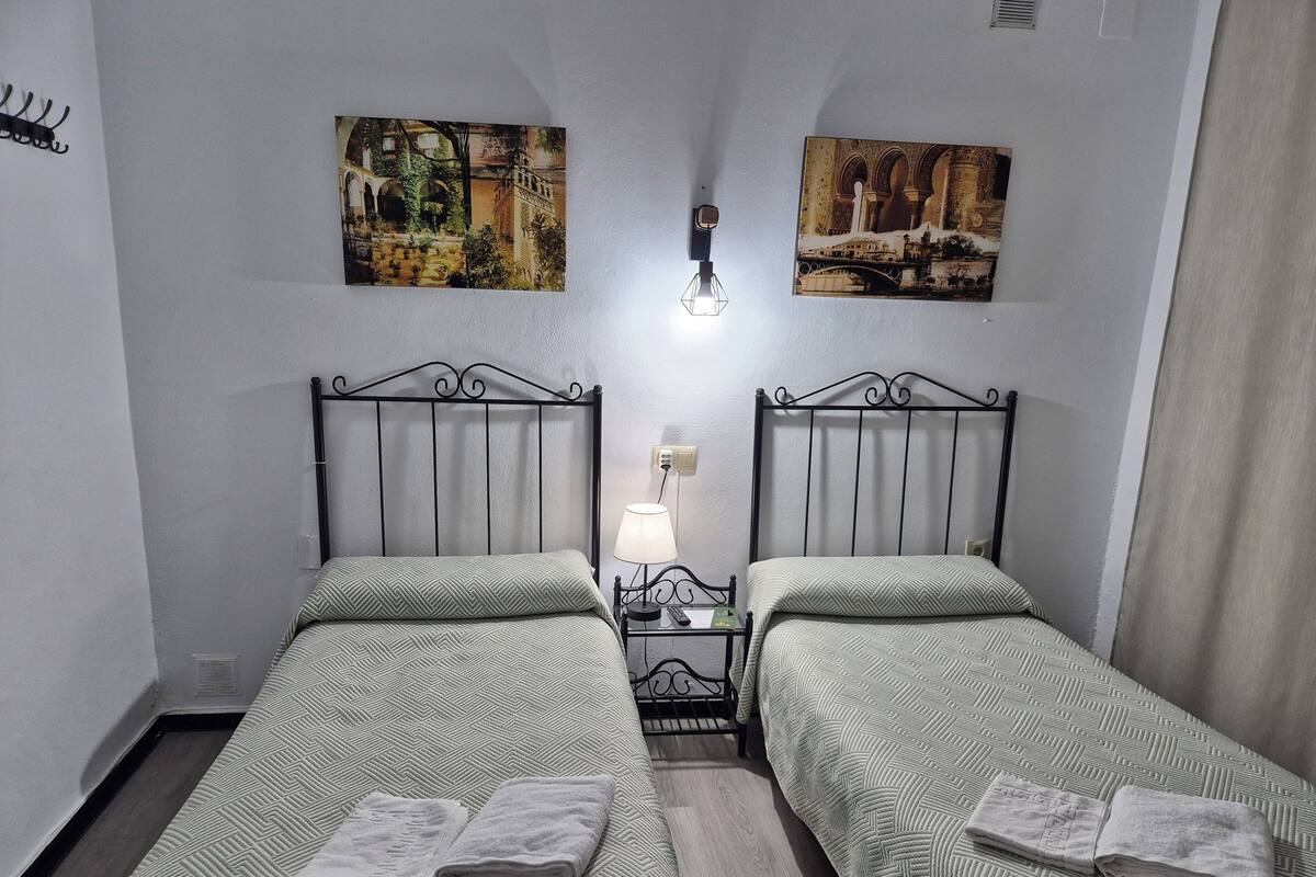 Habitación doble con dos camas, una mesita de noche, una lámpara y dos cuadros en las paredes.