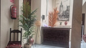 A hallway with a fire extinguisher, a wooden chair, a potted plant, a decorative vase, and a wall-mounted picture. - Pensión Javier (Seville)