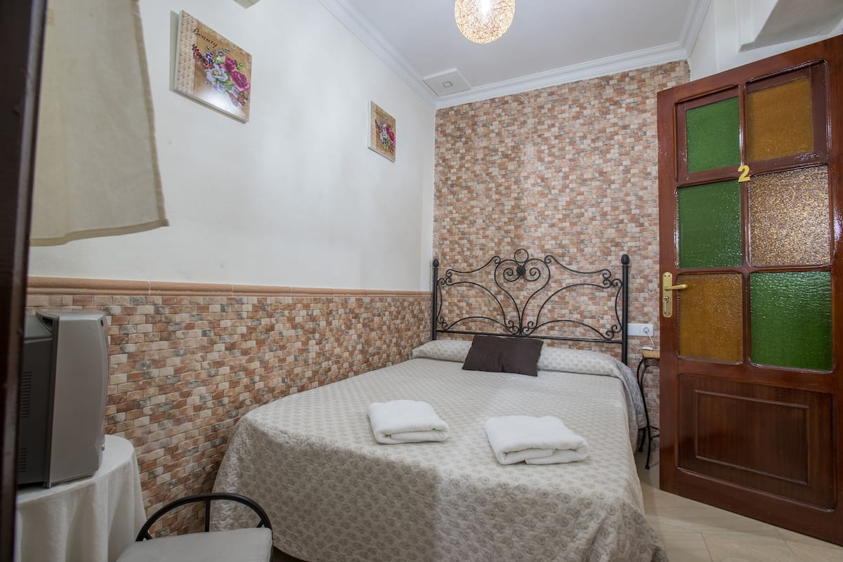 Un dormitorio con pared de ladrillo, una cama con dos almohadas, una mesita de noche con una lámpara y una puerta con un número.