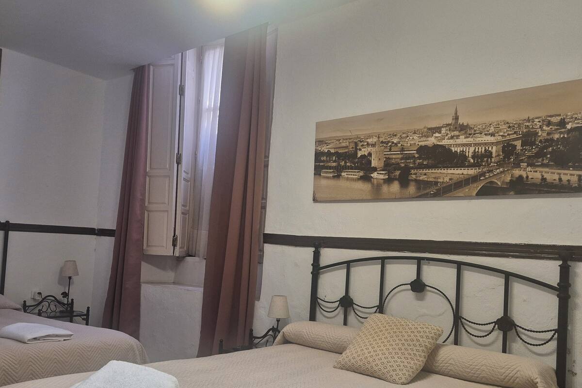 Habitación de hotel con dos camas, vista a un paisaje urbano y un cuadro en la pared.
