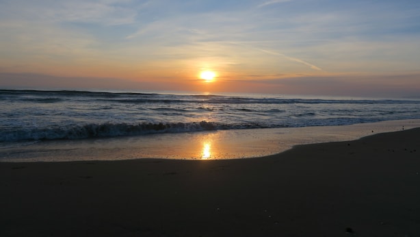 Ein Strand bei Sonnenuntergang mit Wellen und einem wolkenlosen Himmel.