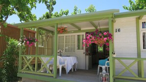 Ein überdachter Außenbereich mit Tisch und Stühlen, einem hängenden Blumenkorb und einem Laternen am Deck.