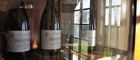 Bottles of Pinot Noir wine in a glass display case with a view of a garden outside.