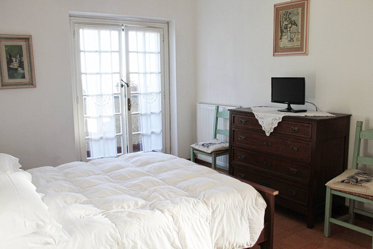 Un dormitorio con cama, cómoda, silla y televisor sobre la cómoda.