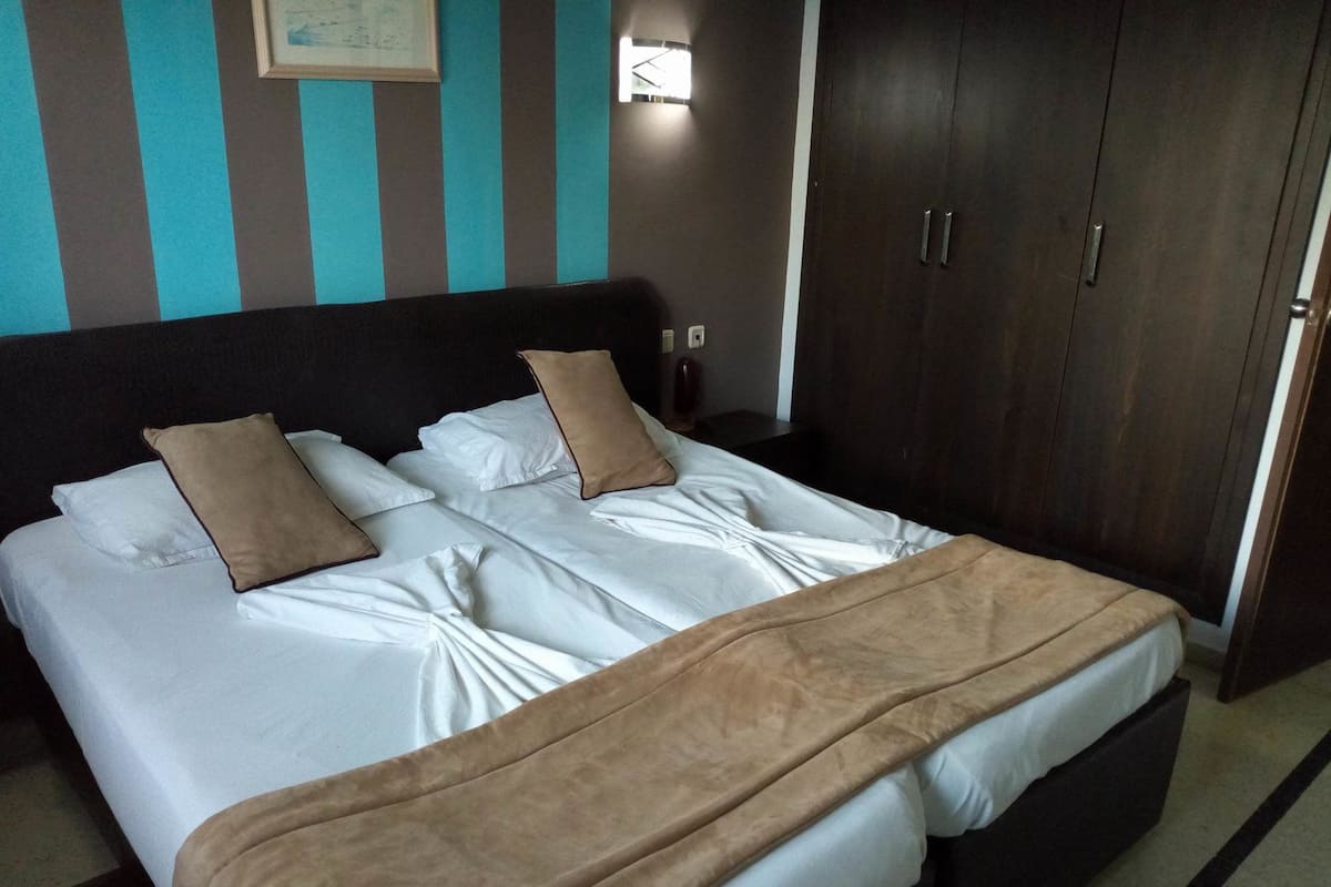Un lit bien fait, avec du linge de lit blanc et des oreillers marron, une tête de lit sombre et une armoire en bois à deux portes.