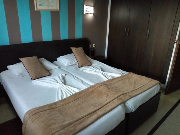 A neatly made bed with white linens and brown pillows, a dark headboard, and a wooden wardrobe with two doors. - Diar Mariem Hotel (Port El Kantaoui)