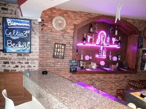 Zona de bar con un letrero de neón, una pared de ladrillo y estantes con botellas.