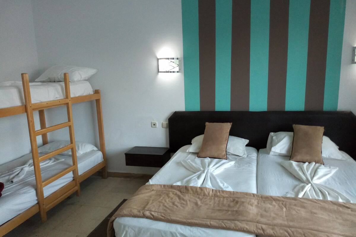 Une chambre avec des lits superposés, une table de chevet et une lampe fixée au mur.