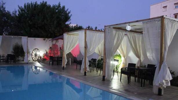 A poolside area with a clear pool, covered seating areas, and a backdrop with a large wheel and red lighting. - Diar Mariem Hotel (Port El Kantaoui)