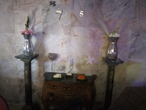 Pared de mármol con los números 8, 7, 5 y 4. Hay dos jarrones con flores sobre pedestales y una pequeña mesa con una flor de loto y un adorno.