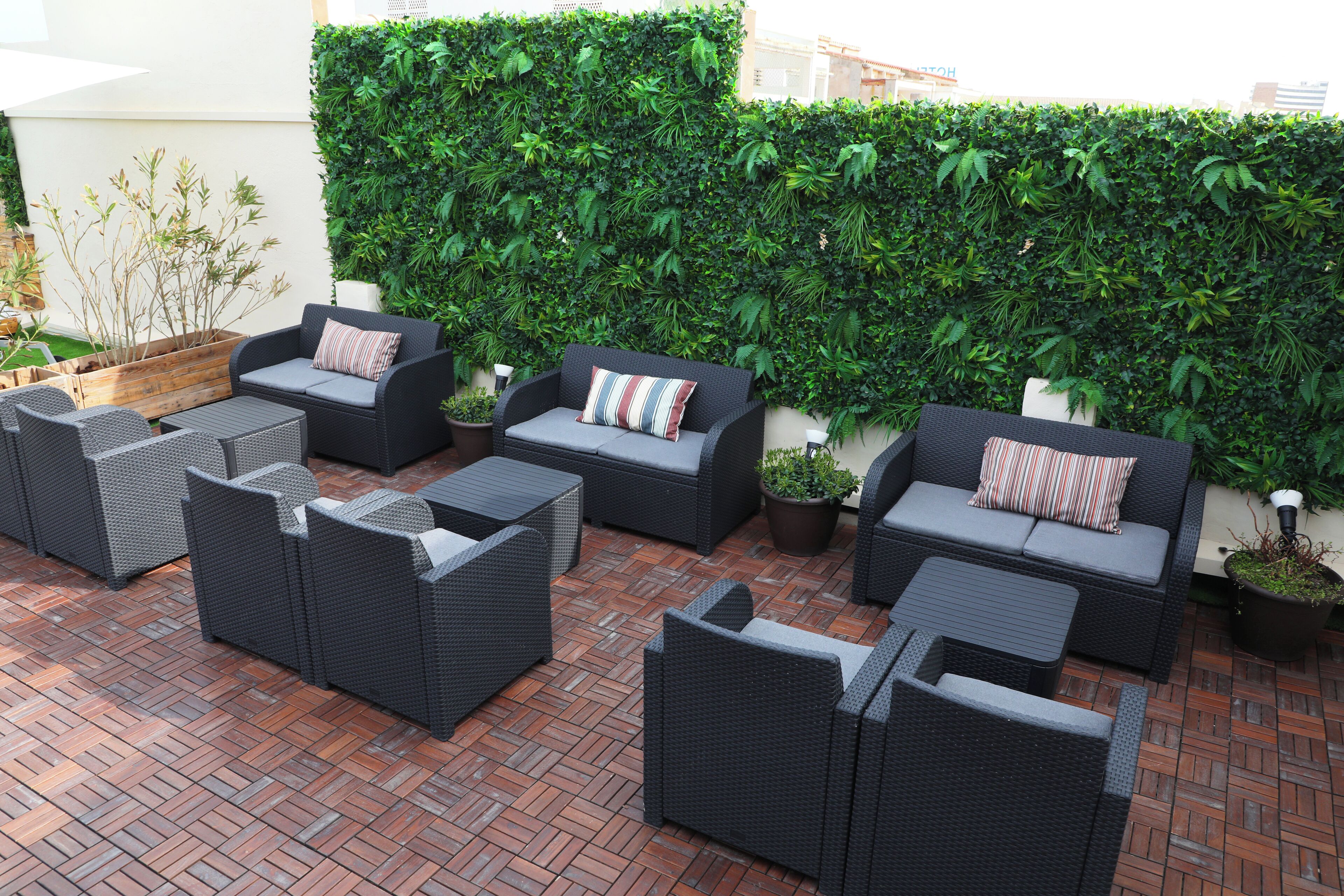 An outdoor seating area with wicker furniture and a green hedge wall.