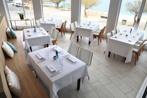 A restaurant with multiple tables set for dining, large windows offering a view of the street and trees, and a clean, modern interior design.