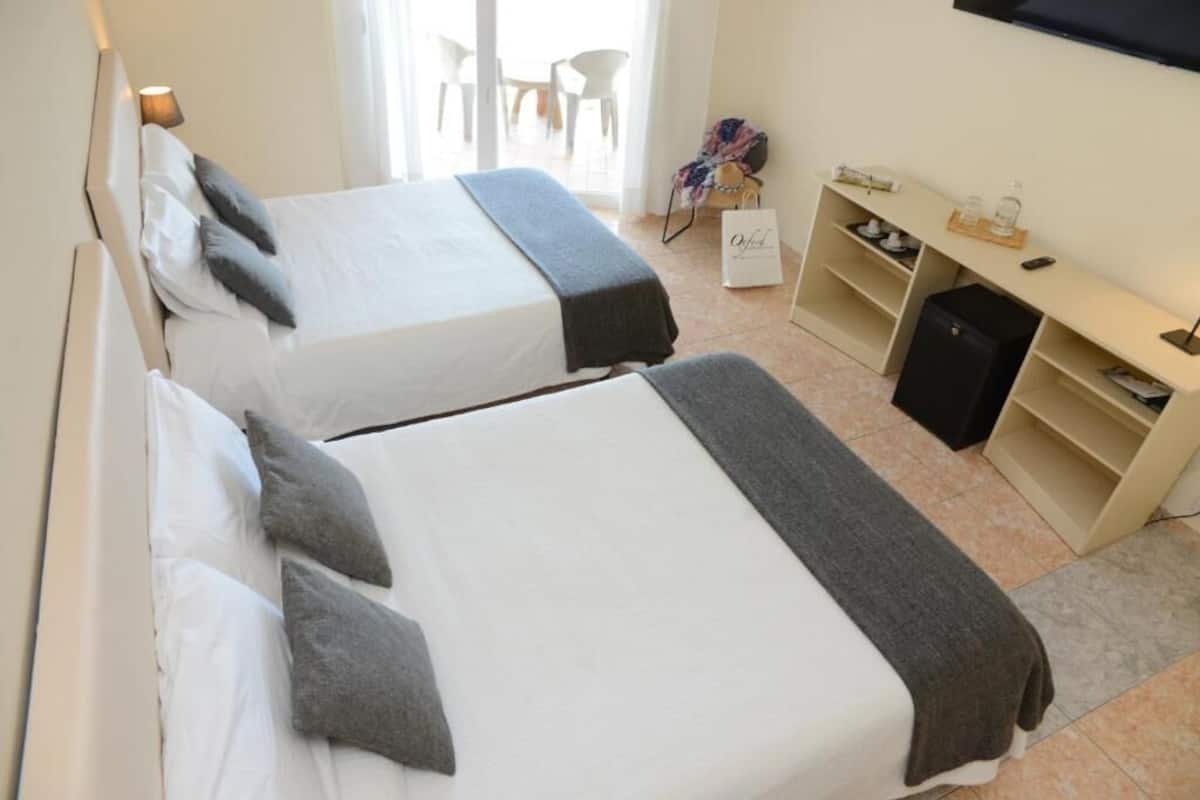 A hotel room with two beds, a desk, a chair, and a TV.