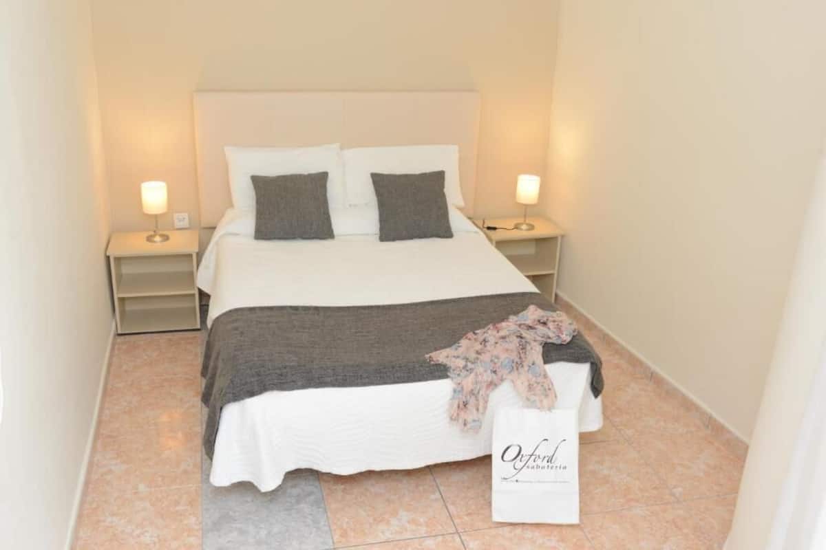 A neatly made bed with white and gray bedding, two bedside lamps, and a sign on the floor.
