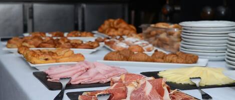 Een buffet met diverse gerechtjes, waaronder gebak, vleeswaren en kaas.