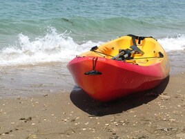A red and yellow kayak on a sandy beach with waves in the background.