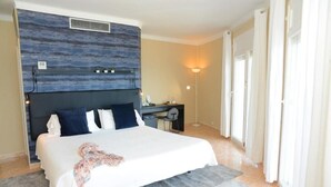 Habitación de hotel con cama, escritorio, silla, lámpara y ventana con cortinas.