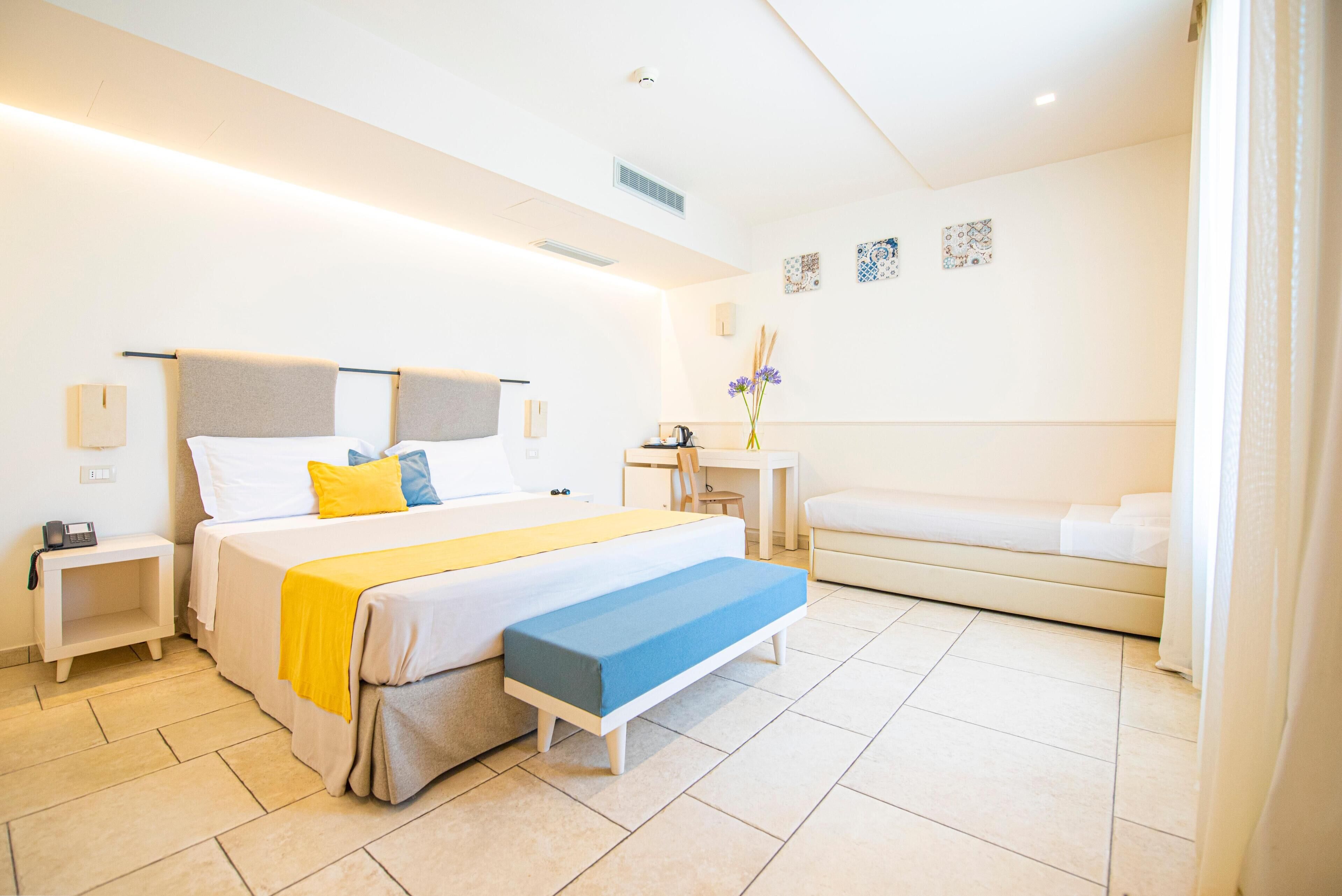 A modern hotel room with a large bed, bedside tables, a desk, and a sofa.