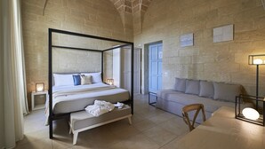 Una cama con dosel, un banco, un sofá y una mesa en una habitación con paredes de piedra y un techo alto.
