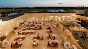 Un área de comedor al aire libre con varias mesas y sillas, rodeada de muros de piedra y luces colgantes.