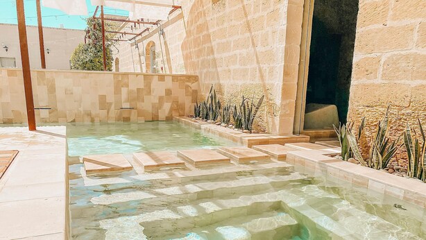 Una piscina con agua cristalina, escalones de piedra y solárium con baldosas.