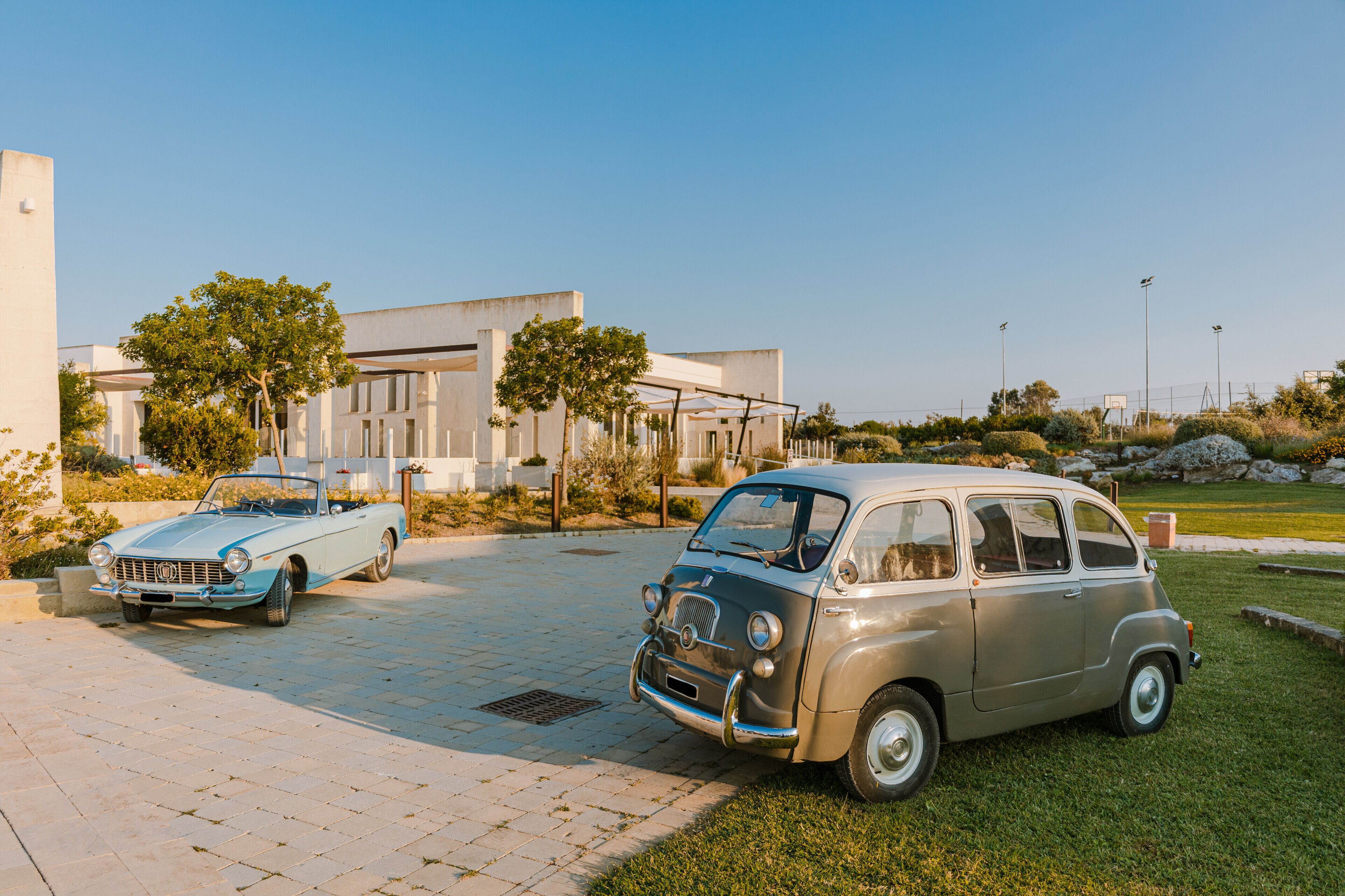 A vintage car parked in a driveway with a modern building in the background.