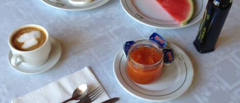 A table with a plate of toast, a slice of watermelon, a cup of coffee, a jar of jam, and a bottle of water.