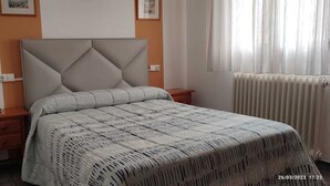 Een slaapkamer met een bed, een nachtkastje, een wandcontactdoos en een radiator.