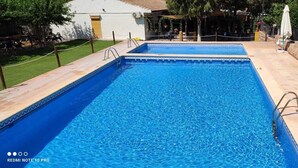 Een rechthoekig zwembad met helderblauw water, omringd door een stenen muur en een betegeld terras.