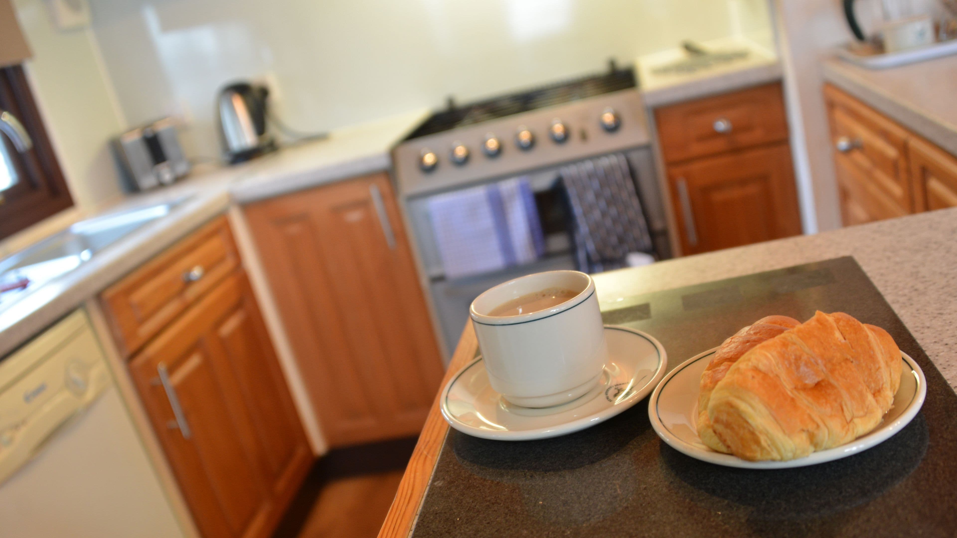 Uma cozinha com armários de madeira, um fogão, uma cafeteira e um croissant num prato.