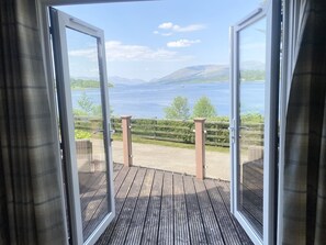 An open sliding glass door leading to a wooden deck with a view of a lake and mountains. - Linnhe Lochside Holidays (Fort William)