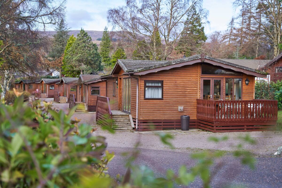 A row of wooden cabins with a gravel driveway and a wooden fence.
