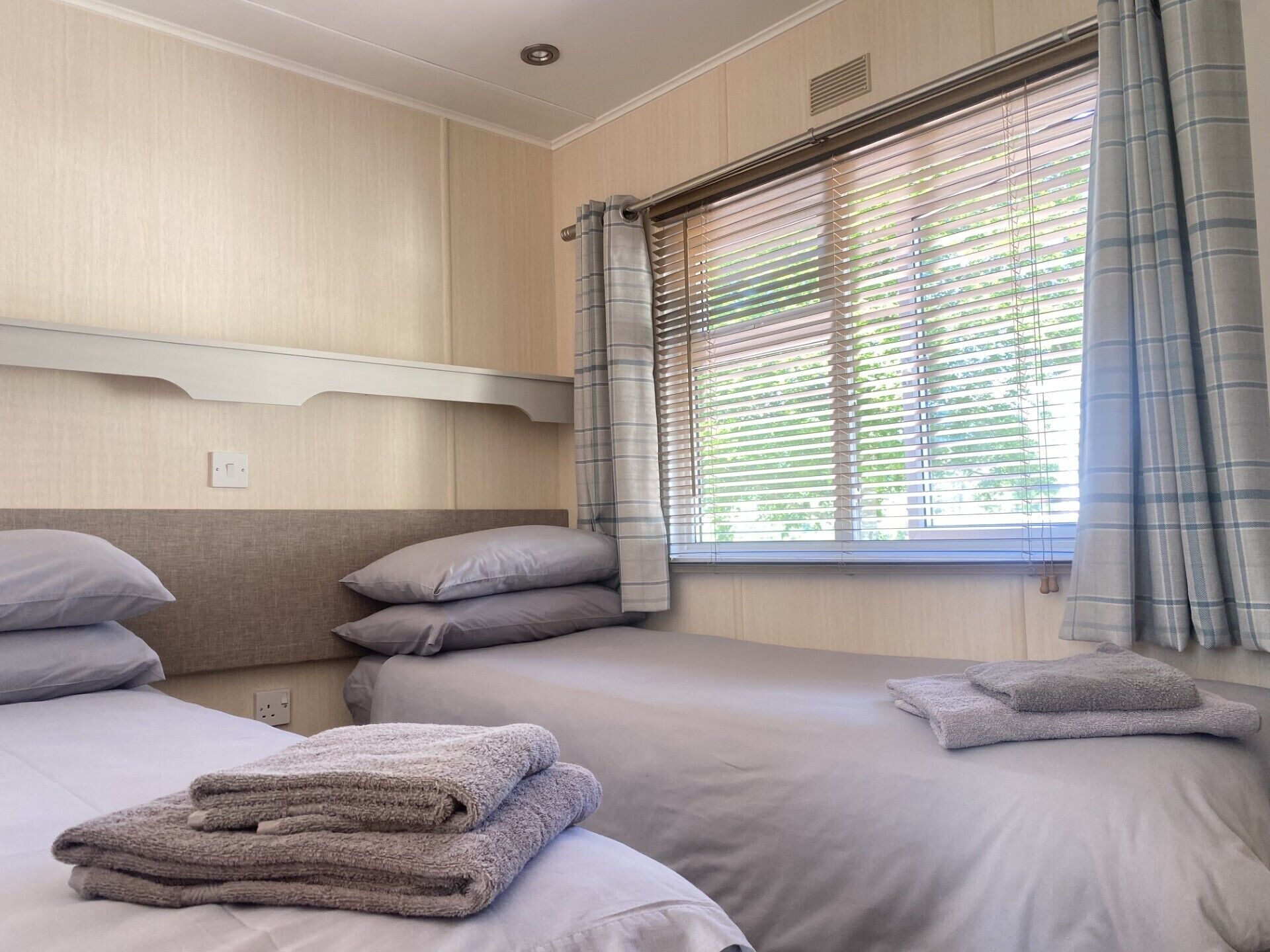 A hotel room with two beds, a window with blinds, and a wall-mounted light fixture.