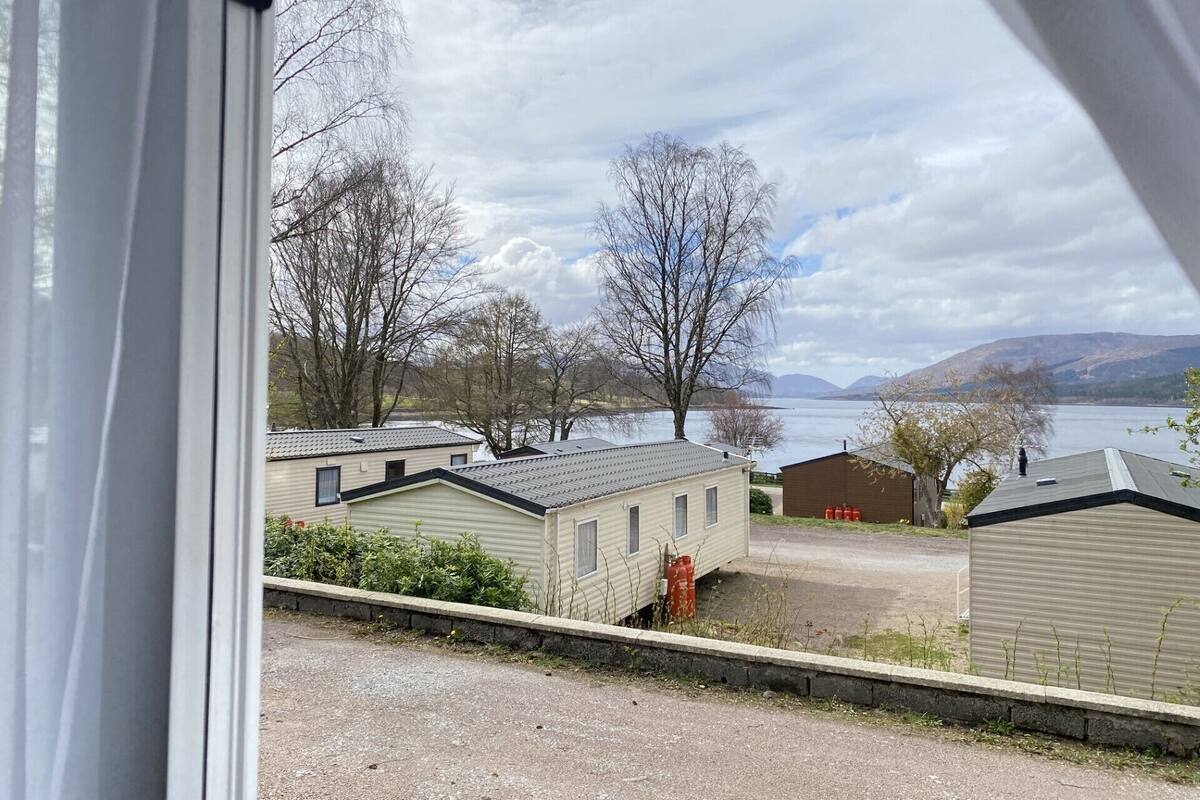 A view of a lakeside area with several mobile homes and a small building, likely a garage or shed, in the foreground.