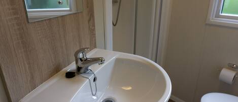 Un baño con lavamanos blanco, un espejo, ducha e inodoro.