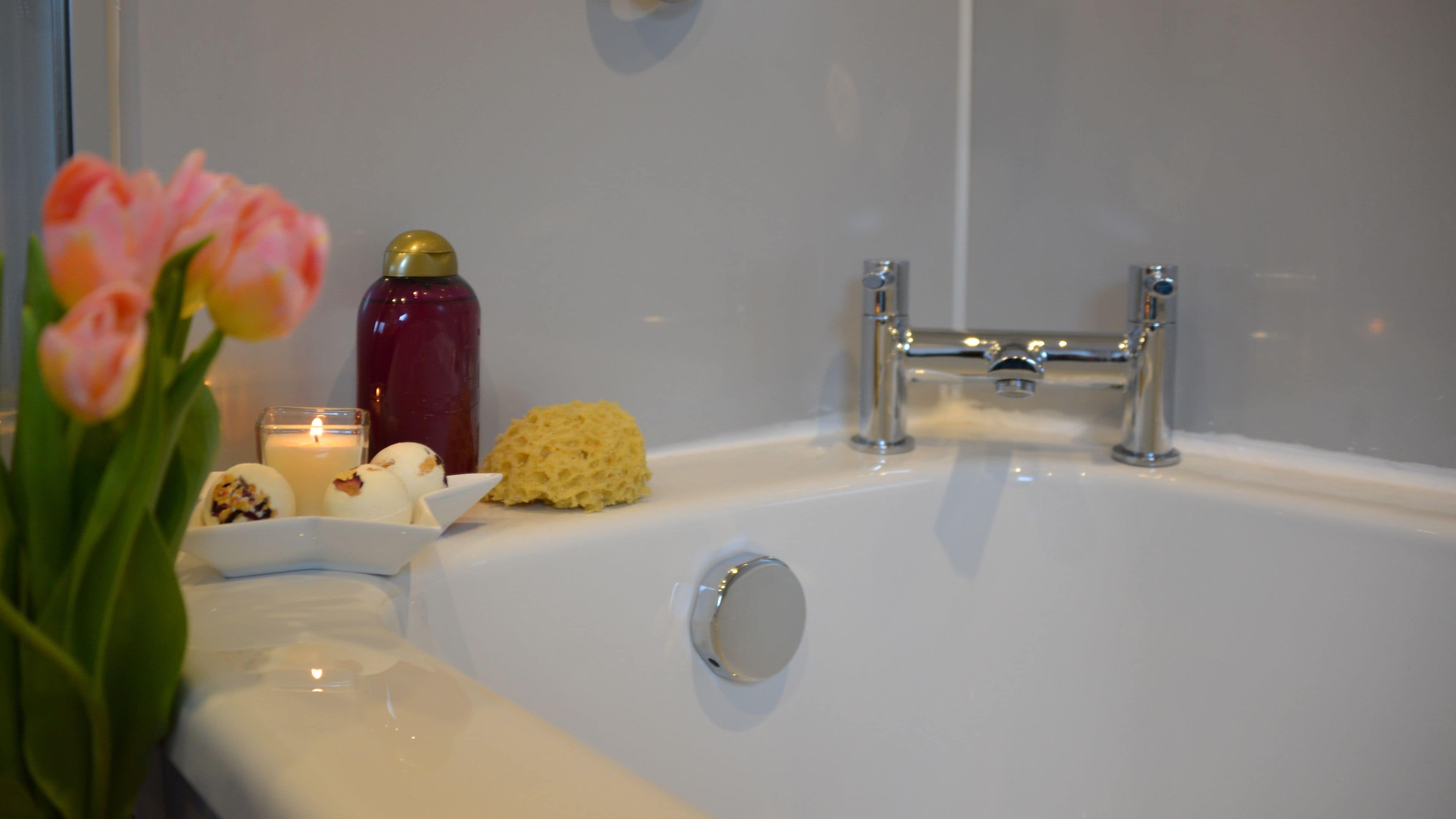 Een badkamer met een bad, een glas water, een kaars en een bloemstuk.
