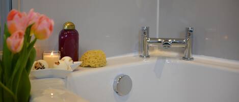 Een badkamer met een bad, een glas water, een kaars en een bloemstuk.