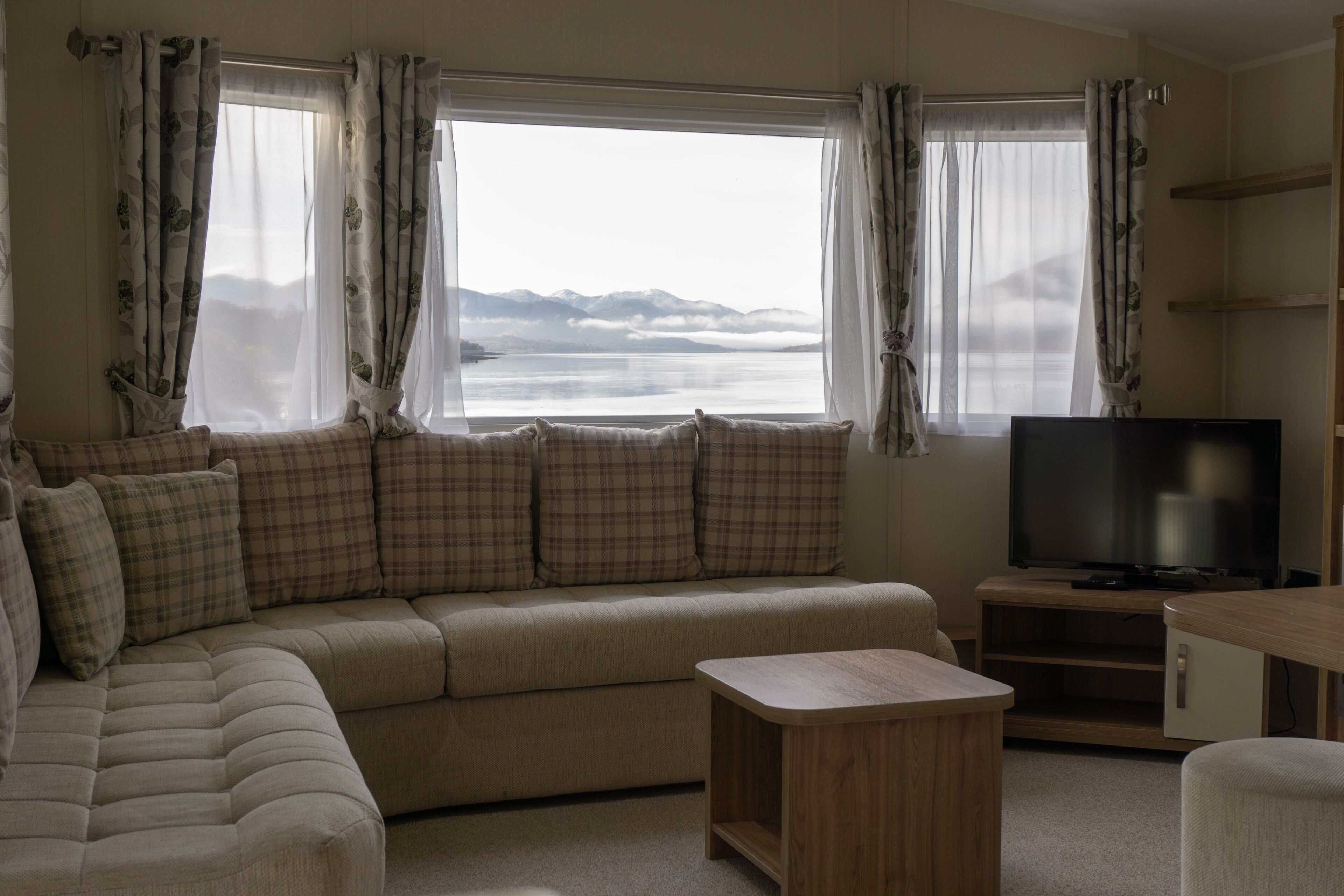 Un salon avec un canapé, un téléviseur et une vue sur les montagnes par la fenêtre.