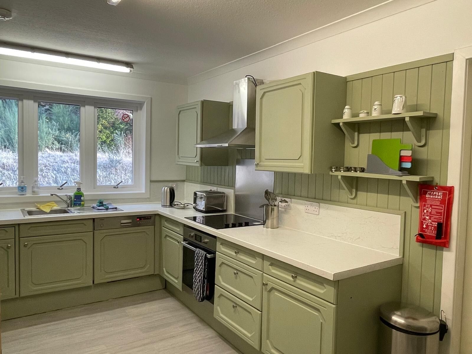 A compact kitchen with a window, built-in appliances, and a fire blanket on the wall.