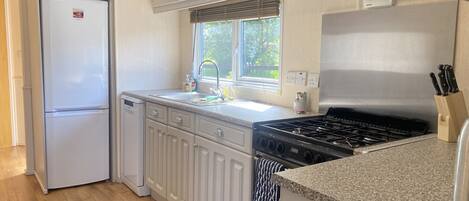 A kitchen with white cabinets, a double-door refrigerator, a stove, and a window with blinds.