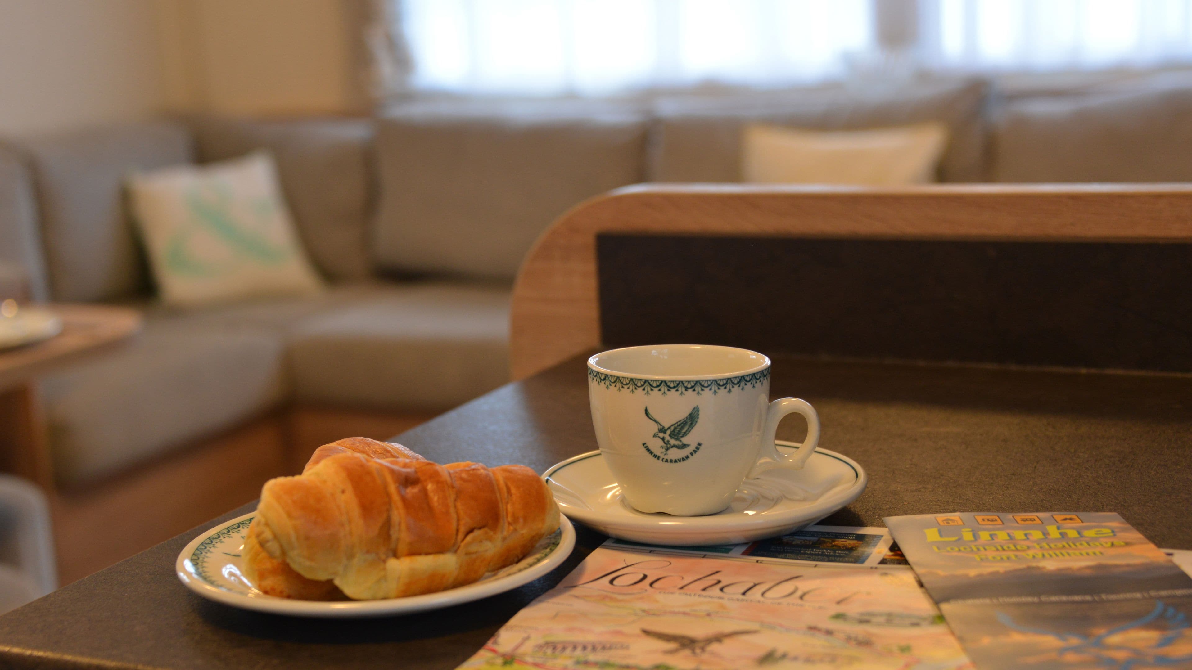 Et spisebord med en croissant, en kop med ørnedesign og en menu.