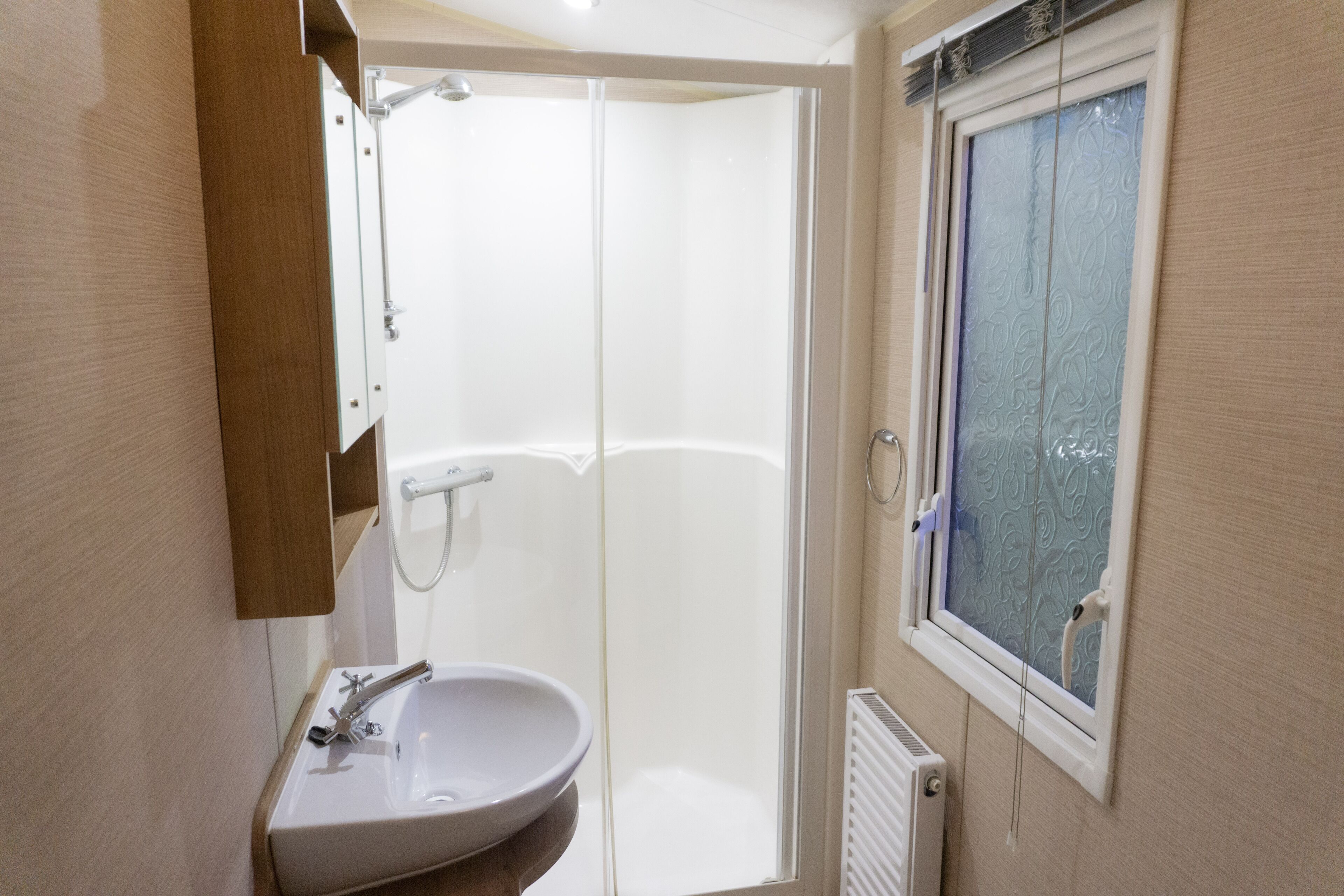 A modern bathroom with a white sink, a glass shower enclosure, and a window with frosted glass.