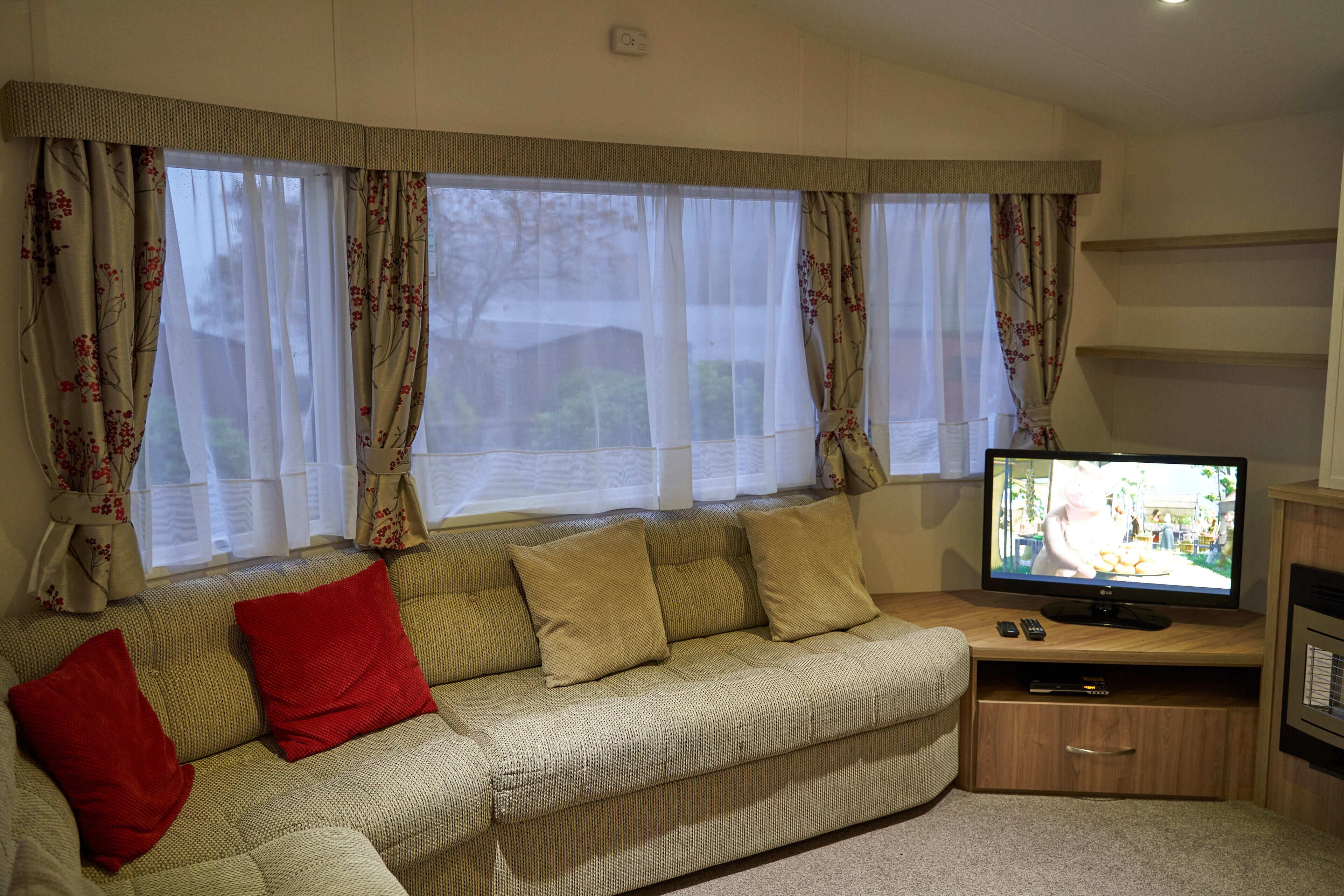 A living room with a sofa, red cushions, a television, and a wooden cabinet.