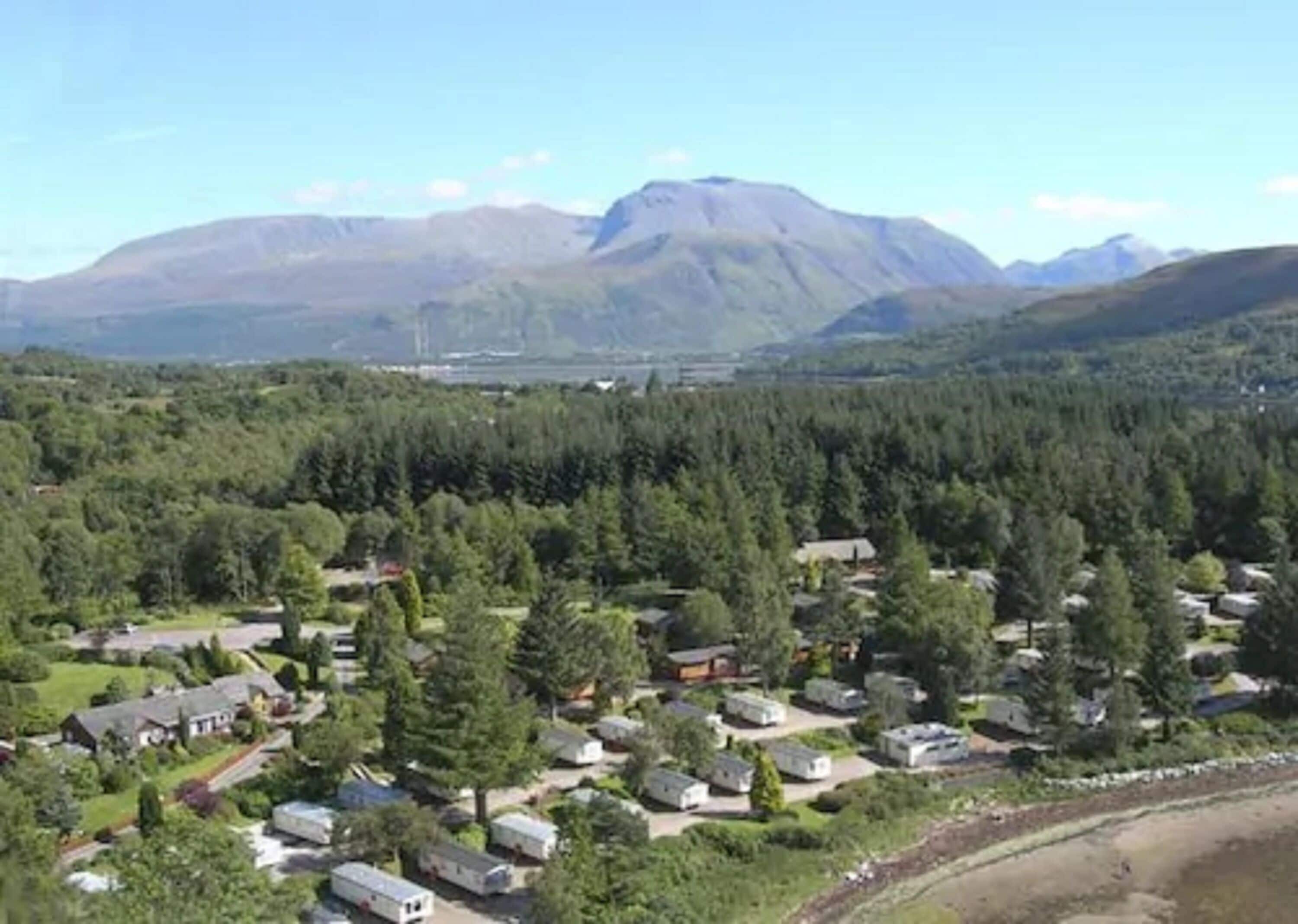 Un quartier résidentiel composé de maisons et de résidences mobiles, entouré d’une forêt dense et avec des montagnes en arrière-plan.