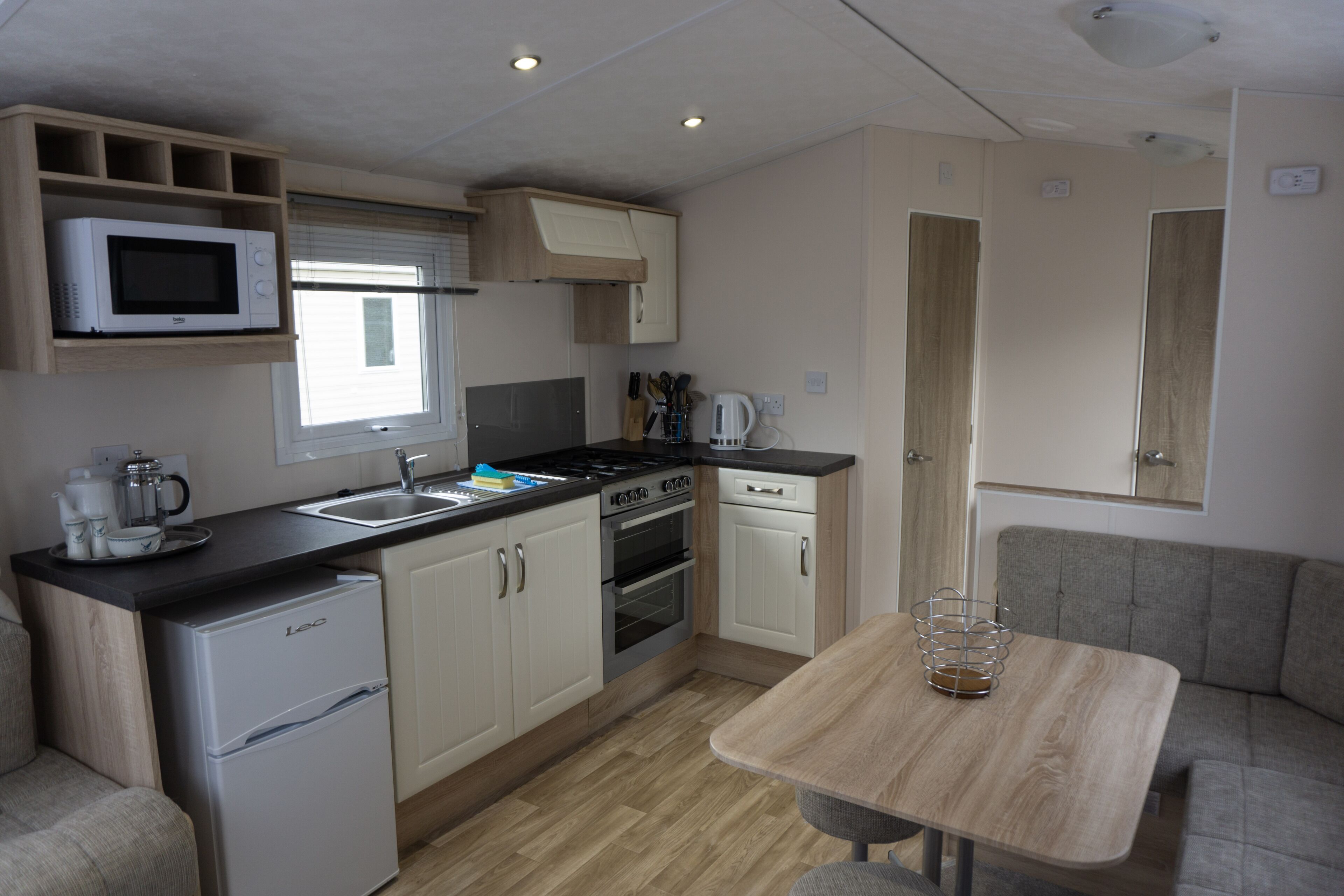 A compact kitchen with a microwave, stove, sink, and refrigerator. There is a dining area with a table and a couch.