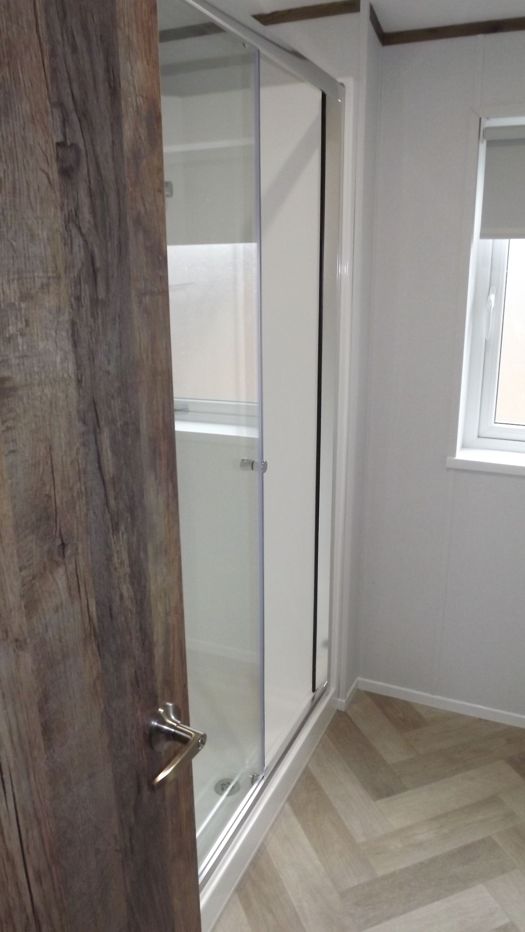 Une pièce dotée d’une porte-fenêtre coulissante donnant sur une zone douche, d’une fenêtre avec vue et d’un plancher à motifs en chevrons.