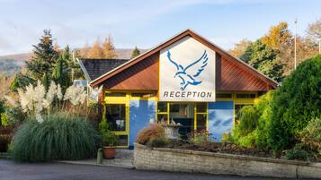A reception building with a bird logo, surrounded by greenery and a mountainous backdrop.