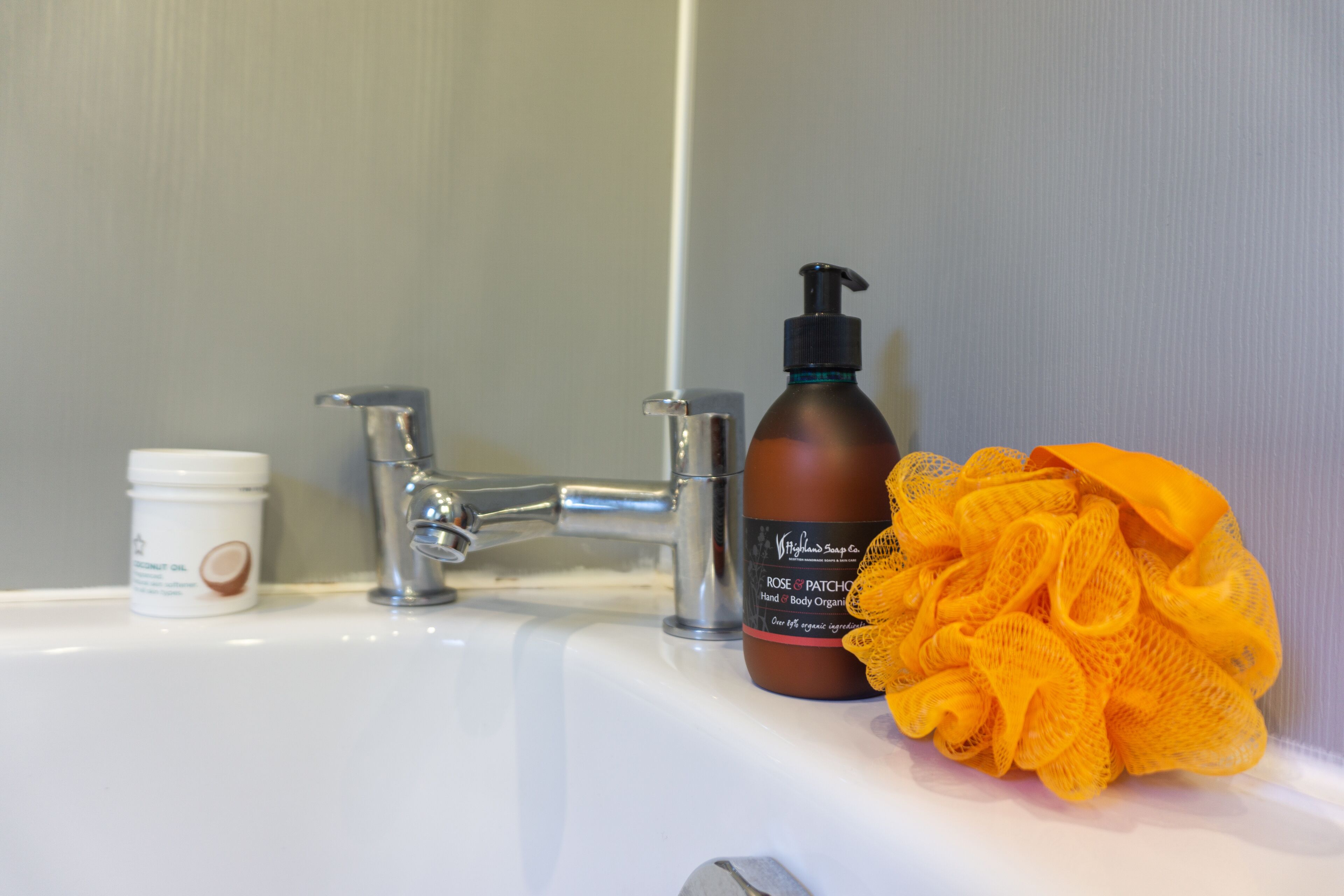 A bathroom sink with a bottle of body lotion and a yellow bath sponge.