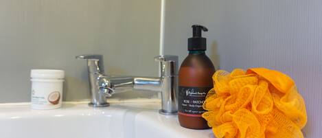 A bathroom sink with a bottle of body lotion and a yellow bath sponge.