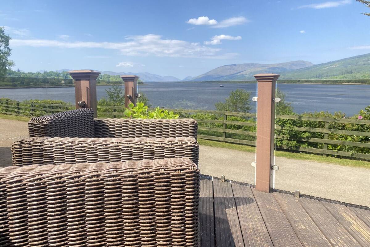 A wooden deck with wicker furniture overlooking a lake.